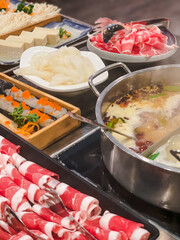 A colorful and inviting hot pot spread featuring thinly sliced beef, tofu, seafood, enoki mushrooms, and a simmering dual broth pot on the table.

