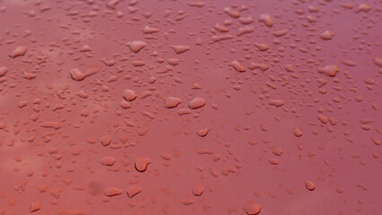 Close-up shot of small raindrops or water droplets on a reddish surface, creating a beautiful and...