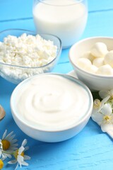 Different fresh dairy products and flowers on light blue wooden table, closeup