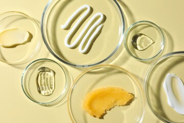 Different cosmetic products in Petri dishes on pale yellow background, flat lay