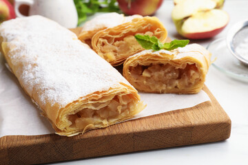 Tasty apple strudels with powdered sugar and mint on white table, closeup