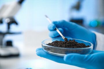 Scientist taking soil sample for research at white table in laboratory, closeup