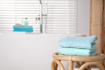 Stack of colorful towels on table near tub in bathroom, space for text