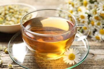 Aromatic tea in glass cup and chamomile flowers on wooden table, closeup