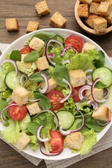 Delicious salad with croutons and vegetables on wooden table, flat lay