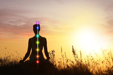 Woman meditating in Lotus pose in nature at sunrise. Seven chakras glowing