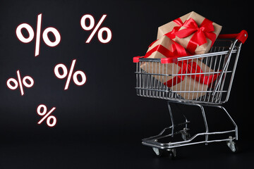 Percent signs near shopping cart with gift boxes against black background. Hot sale, special offer
