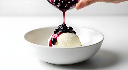 Vanilla ice cream scoop topped with fresh blueberry sauce and whole berries in a white bowl