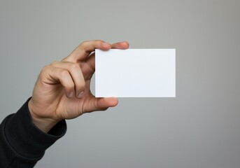 Obraz premium Hand holding a blank white business card against a neutral gray background