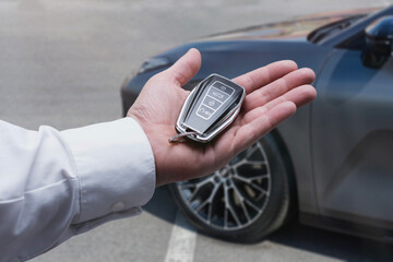 Male hand holding car key fob near luxury vehicle on a parking.