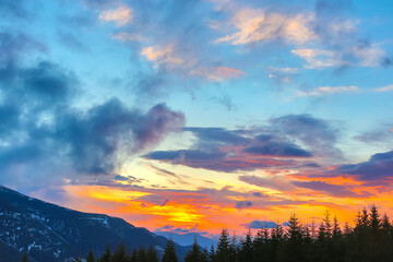 Stunning sunset highlights mountains and trees in a vibrant sky filled with colors