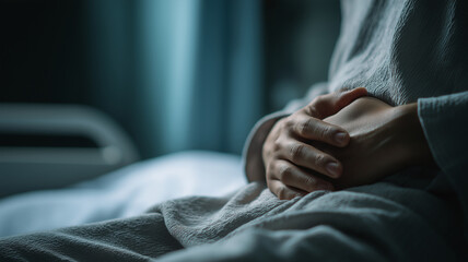 Person sitting on bed, gripping their stomach in pain, wearing gray robe in dimly lit room. atmosphere is somber and reflective