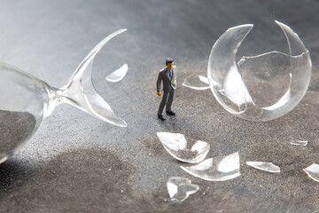 Miniature businessman stands among shattered glass pieces following a mishap