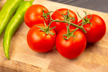 Fresh tomatoes and green peppers on a wooden cutting board ready for cooking