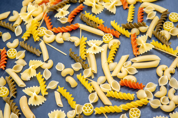 Colorful assortment of pasta shapes scattered on a blue surface ready for cooking