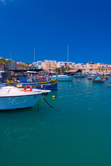 Obraz premium Malta Republic, Malta Island. 28. 06.2023. Marsaxlokk city, The harbour and coloured traditional boats on a hot sunny day.