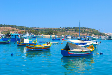 Fototapeta premium Marsaxlokk, Malta - July 07, 2021: The harbour of Marsaxlokk with the traditional and colourful Luzzu boats. This was during the Covid 19 pandemic on a hot sunny summers afternoon.