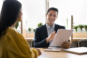 Smiling Hispanic businessman holds stack of papers reviewing written information, providing...