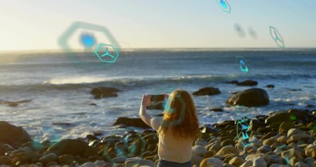Woman raising smartphone over ocean and activating AR overlays for monitoring environmental data - Powered by Adobe