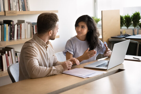 Two multinational colleagues lead project-related discussion met in coworking office using laptop. Indian woman presenting idea, clarifying point, share creative ideas during briefing with team member - Powered by Adobe
