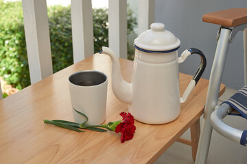 Cozy Outdoor Setting With a White Teapot, a Cup, and a Flower on a Wooden Table Next to a Relaxed Chair