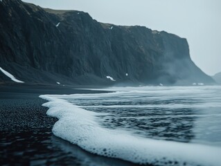 Naklejka premium Foamy waves lapping at a black sand beach, dramatic cliffs loom in the background