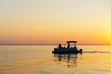 Enjoy a serene sunset cruise on a pontoon boat, gliding across a calm lake. This scene captures relaxation and leisure, perfect for peaceful getaways and tourism. © Ilja