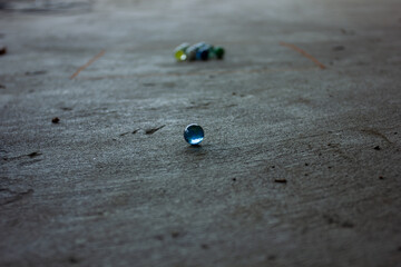 Close-up of a single blue glass marble on a concrete floor during a marble game. Concept of games, concentration, and childhood.