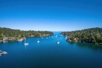 Obraz premium Aerial View of Sailboats Anchored in Calm Bay Surrounded by Forested Islands on Sunny Day