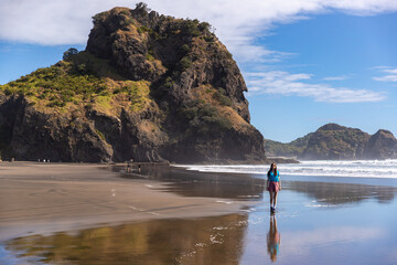 Girl walks along iconic Piha Beach, admiring dramatic volcanic rock formations in the Waitākere...