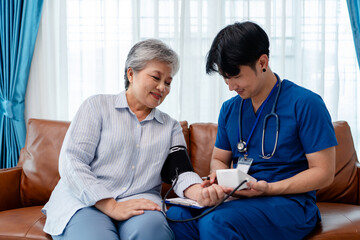 Obraz premium asian senior woman using blood pressure monitor digital device instructed by physiotherapist. home caregiver nurse visit retirement patient for health check up recovery process medical service