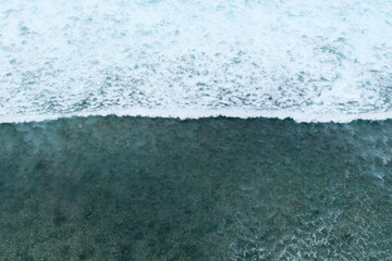 Aerial view of foamy blue waves breaking onto a shallow shoreline, capturing the motion and texture...