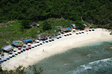 Fototapeta premium Aerial view of a quiet tropical beach in Bali with colorful umbrellas, white sand, and turquoise water near lush greenery.