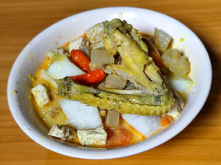 Traditional Indonesian vegetable lontong dish. Lontong opor ayam with sliced chayote, carrots, tofu and sliced red chilies, served in a white ceramic bowl on a wooden table.