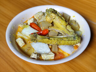 Traditional Indonesian vegetable lontong dish. Lontong opor ayam with sliced chayote, carrots, tofu and sliced red chilies, served in a white ceramic bowl on a wooden table.