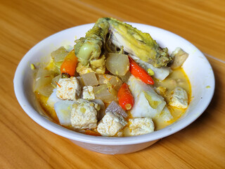 Traditional Indonesian vegetable lontong dish. Lontong opor ayam with sliced chayote, carrots, tofu and sliced red chilies, served in a white ceramic bowl on a wooden table.