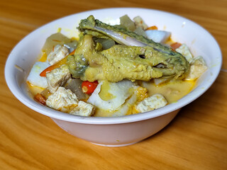 Traditional Indonesian vegetable lontong dish. Lontong opor ayam with sliced chayote, carrots, tofu and sliced red chilies, served in a white ceramic bowl on a wooden table.