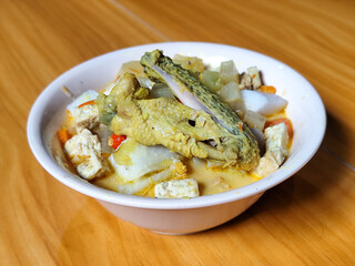 Traditional Indonesian vegetable lontong dish. Lontong opor ayam with sliced chayote, carrots, tofu and sliced red chilies, served in a white ceramic bowl on a wooden table.
