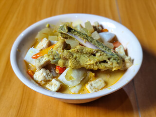 Traditional Indonesian vegetable lontong dish. Lontong opor ayam with sliced chayote, carrots, tofu and sliced red chilies, served in a white ceramic bowl on a wooden table.
