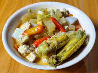 Traditional Indonesian vegetable lontong dish. Lontong opor ayam with sliced chayote, carrots, tofu and sliced red chilies, served in a white ceramic bowl on a wooden table.
