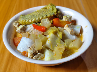 Traditional Indonesian vegetable lontong dish. Lontong opor ayam with sliced chayote, carrots, tofu and sliced red chilies, served in a white ceramic bowl on a wooden table.
