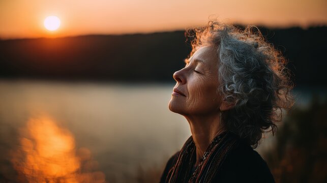 Mature woman meditates outdoors, sunset behind her, eyes closed, face serene. Use this for themes of aging gracefully, mindfulness, or enjoying nature.