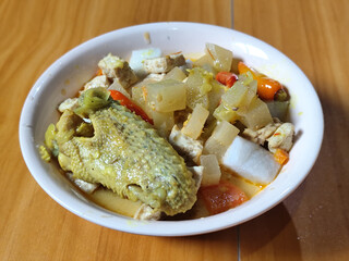 Traditional Indonesian vegetable lontong dish. Lontong opor ayam with sliced chayote, carrots, tofu and sliced red chilies, served in a white ceramic bowl on a wooden table.