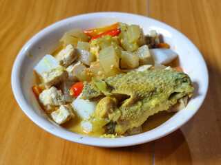 Traditional Indonesian vegetable lontong dish. Lontong opor ayam with sliced chayote, carrots, tofu and sliced red chilies, served in a white ceramic bowl on a wooden table.