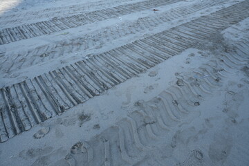 Close-up view of beach sand showing parallel tire marks and scattered footprints, capturing texture...