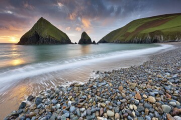Coastal scene at sunrise with dramatic rock formations and a pebble beach