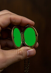 A close-up shot of a hand holding an open vintage bronze locket with two empty green screen frames ready for content insertion