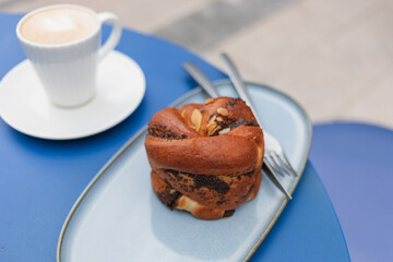Close-up of a poppy-flavored brioche and latte coffee in elegant white cups on a blue table.