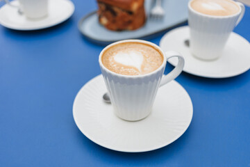 Cappuccino coffee in beautiful, elegant white cups with pastries placed on a blue table.