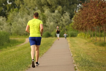 A man in a yellow and blue sports uniform runs on a park alley. Maintaining fitness in adulthood....